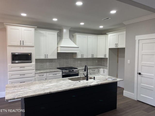 kitchen featuring decorative backsplash, premium range hood, stainless steel appliances, a kitchen island with sink, and white cabinetry