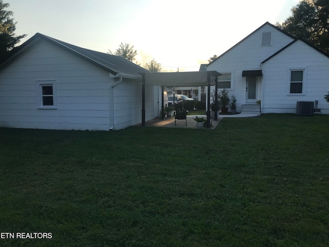 back house at dusk featuring central AC, a patio area, and a yard