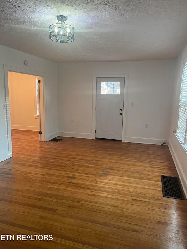 entryway with an inviting chandelier, light wood-type flooring, and a textured ceiling