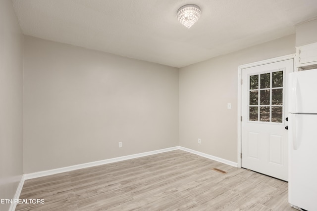 spare room featuring light wood-type flooring and a textured ceiling