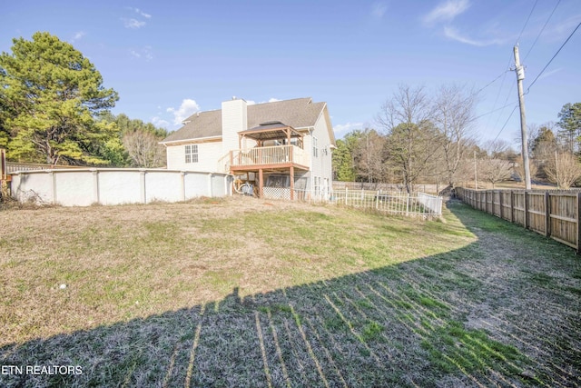 rear view of property featuring an outdoor pool, a lawn, a fenced backyard, a chimney, and a wooden deck