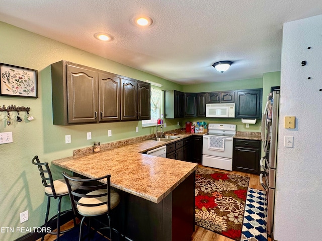 kitchen with kitchen peninsula, white appliances, sink, and a breakfast bar area