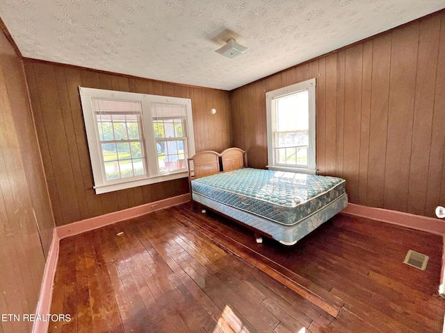 bedroom featuring a textured ceiling, wooden walls, and dark hardwood / wood-style floors