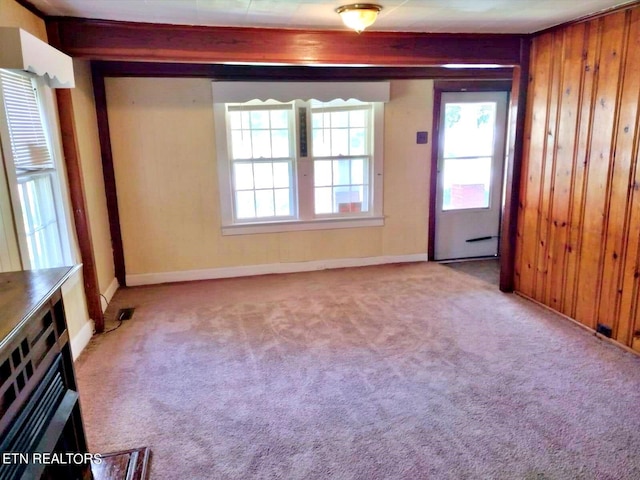 unfurnished room with beam ceiling, wood walls, and light colored carpet