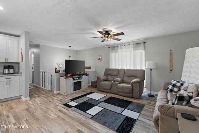 living room with light hardwood / wood-style floors, ceiling fan, and a textured ceiling