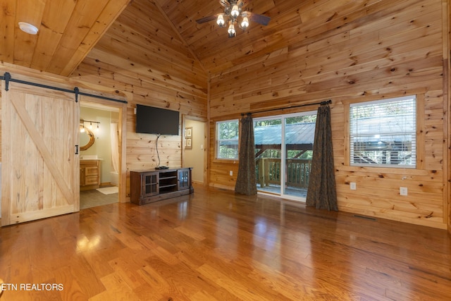 unfurnished living room with wood ceiling, ceiling fan, a barn door, high vaulted ceiling, and wood walls