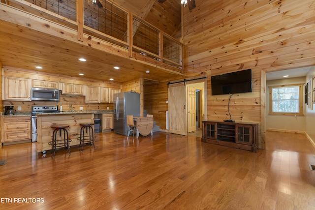 kitchen featuring stainless steel appliances, a barn door, a towering ceiling, a kitchen bar, and light brown cabinetry