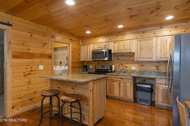 kitchen featuring appliances with stainless steel finishes, light stone counters, wooden walls, and a kitchen breakfast bar