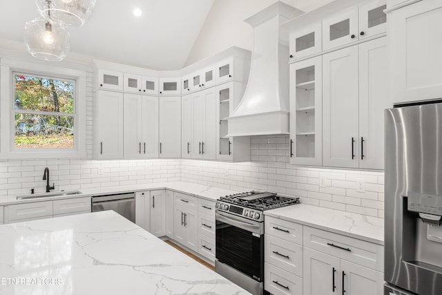 kitchen with lofted ceiling, custom exhaust hood, a sink, white cabinets, and appliances with stainless steel finishes