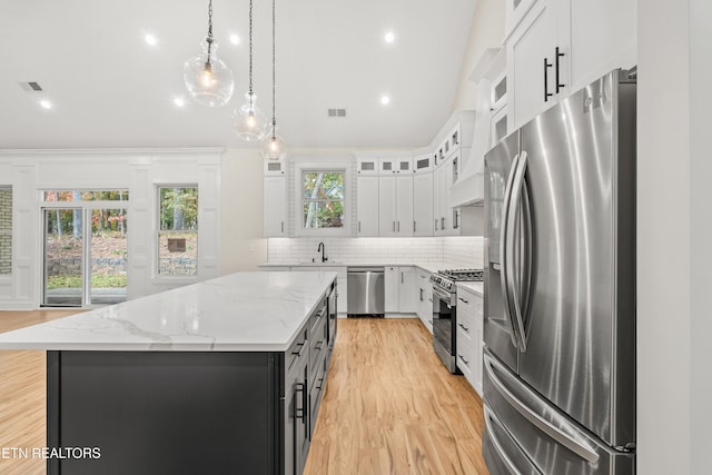 kitchen featuring light wood-style flooring, a kitchen island, stainless steel appliances, white cabinets, and decorative backsplash