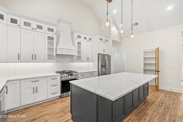 kitchen with light wood finished floors, a center island, custom exhaust hood, white cabinets, and stainless steel appliances