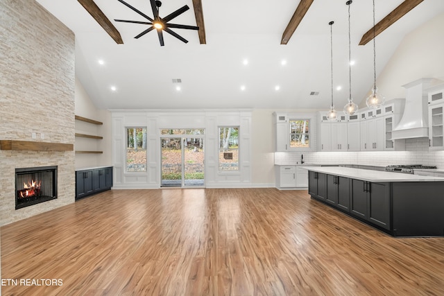 unfurnished living room featuring visible vents, ceiling fan, beamed ceiling, light wood-type flooring, and a stone fireplace