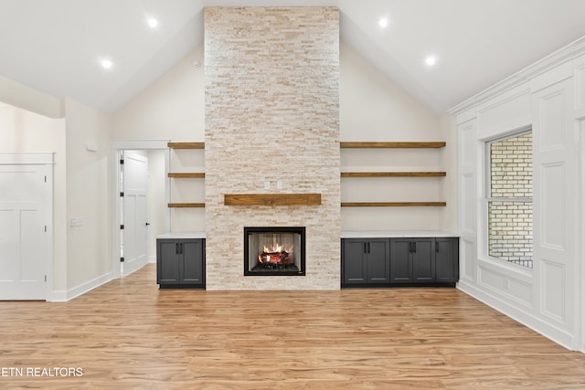 unfurnished living room with light wood finished floors, baseboards, a stone fireplace, recessed lighting, and high vaulted ceiling