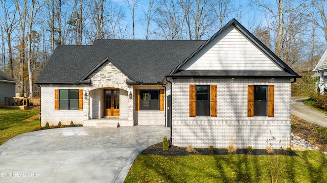 view of front facade with a front lawn, brick siding, driveway, and a shingled roof