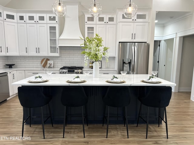 kitchen with premium range hood, appliances with stainless steel finishes, ornamental molding, and white cabinetry