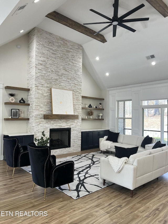 living room with a stone fireplace, beamed ceiling, and visible vents