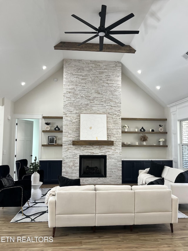 living area featuring visible vents, beamed ceiling, a stone fireplace, wood finished floors, and high vaulted ceiling