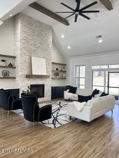 living area featuring visible vents, light wood-style floors, a stone fireplace, and a healthy amount of sunlight