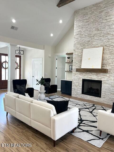 living area featuring decorative columns, beam ceiling, a stone fireplace, and wood finished floors