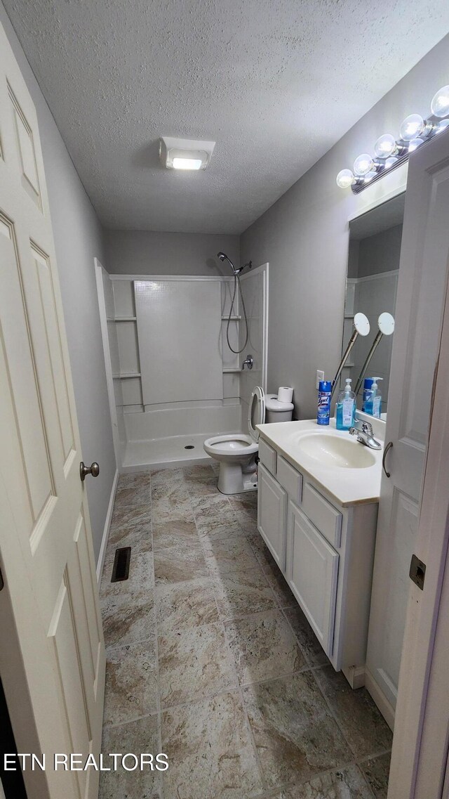 bathroom with toilet, vanity, a shower, and a textured ceiling