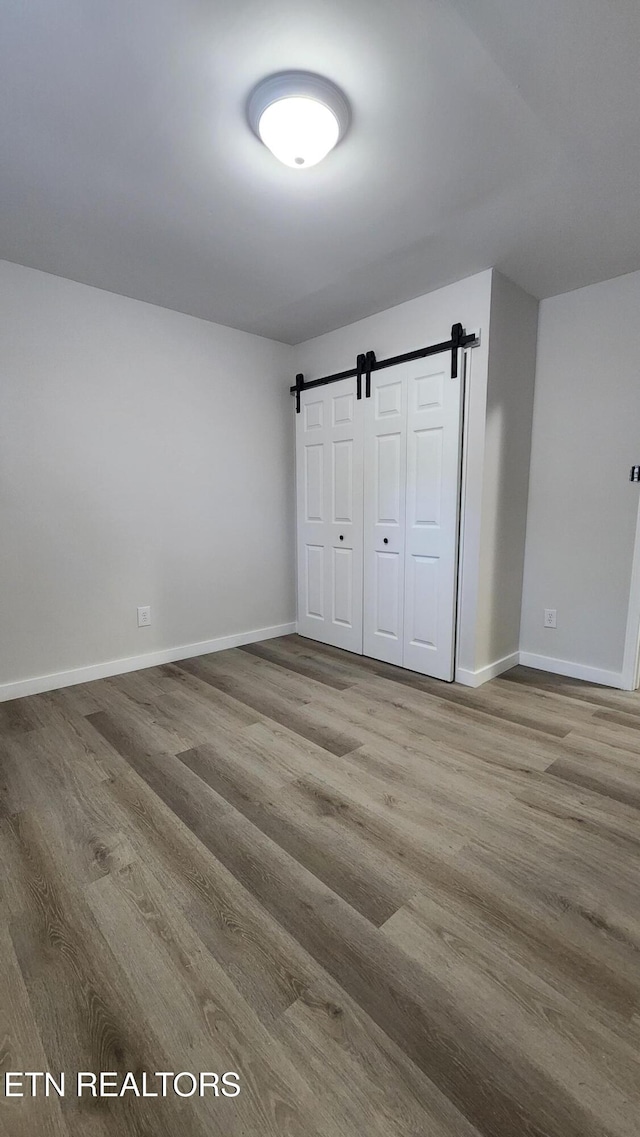 unfurnished bedroom featuring a barn door, a closet, wood finished floors, and baseboards