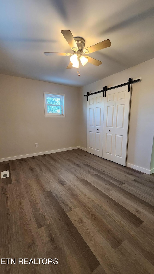 unfurnished bedroom with dark wood finished floors, visible vents, a barn door, a ceiling fan, and baseboards