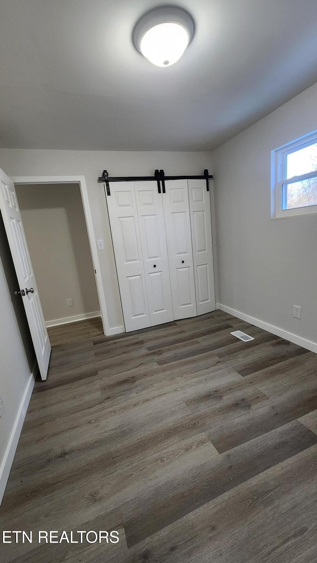 unfurnished bedroom featuring dark wood-style floors, a barn door, baseboards, and a closet