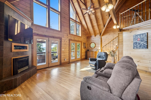 living room featuring light wood-type flooring, wood walls, beam ceiling, high vaulted ceiling, and french doors