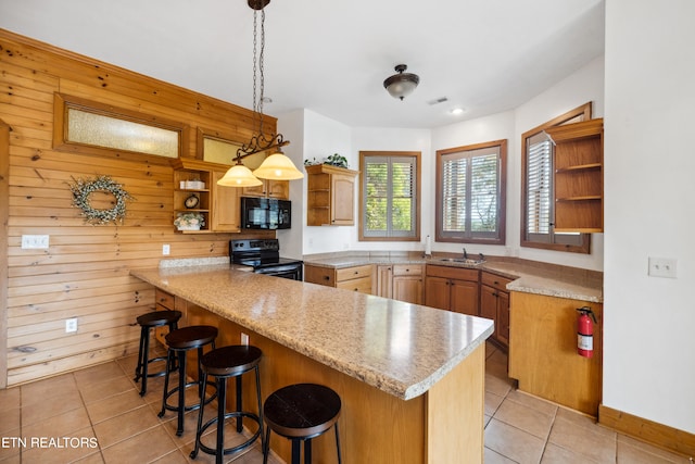 kitchen featuring a breakfast bar, kitchen peninsula, pendant lighting, black appliances, and wooden walls