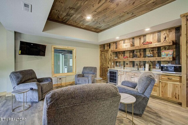 living area with wood ceiling, light wood-type flooring, a tray ceiling, indoor wet bar, and beverage cooler