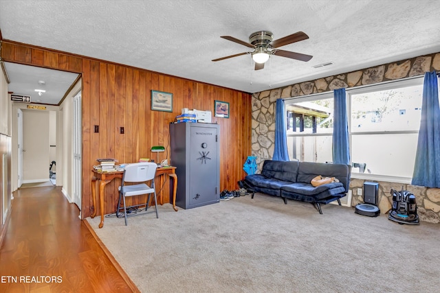 living room with wood walls, wood-type flooring, ceiling fan, and a textured ceiling