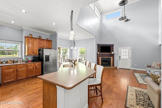 kitchen featuring light hardwood / wood-style floors, stainless steel fridge with ice dispenser, sink, a kitchen bar, and a center island with sink