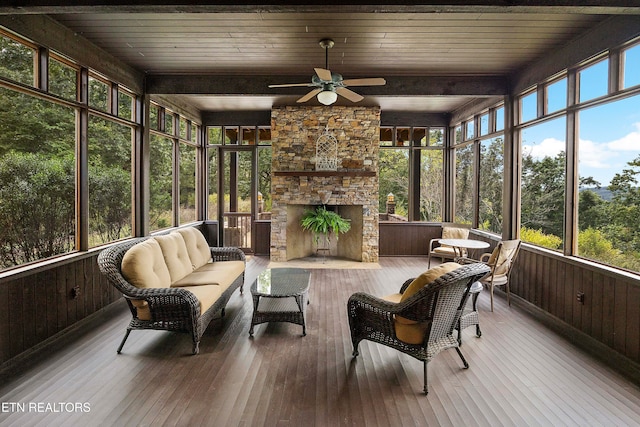 sunroom featuring wooden ceiling, a stone fireplace, ceiling fan, and beamed ceiling