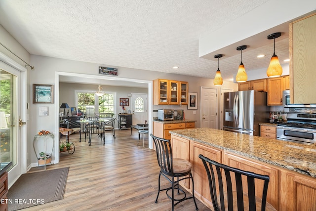 kitchen with appliances with stainless steel finishes, light hardwood / wood-style floors, light stone countertops, pendant lighting, and a textured ceiling