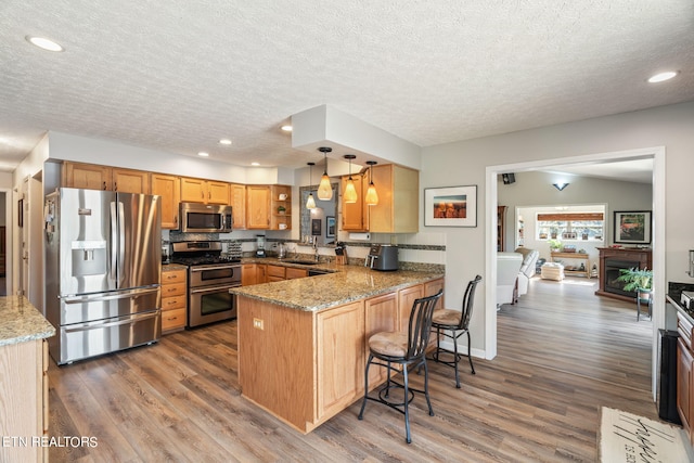 kitchen featuring appliances with stainless steel finishes, kitchen peninsula, pendant lighting, dark hardwood / wood-style floors, and sink