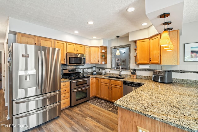 kitchen featuring light stone counters, hanging light fixtures, sink, wood-type flooring, and appliances with stainless steel finishes