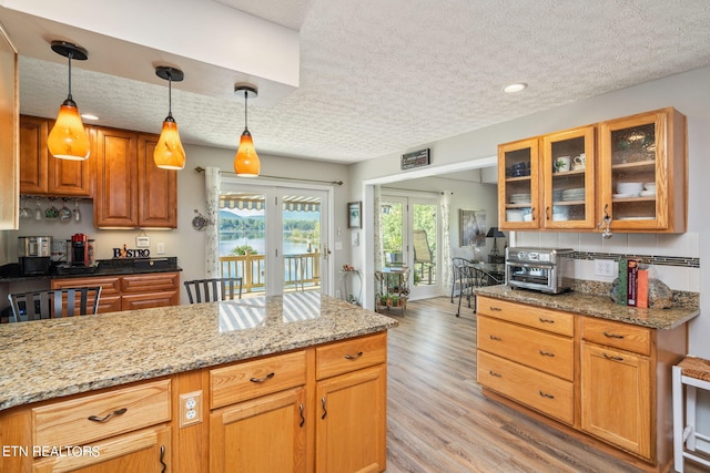 kitchen featuring a textured ceiling, hanging light fixtures, light hardwood / wood-style floors, and light stone countertops