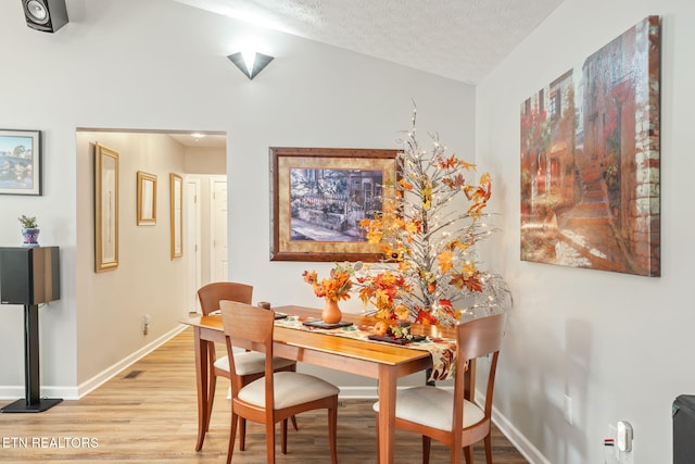 dining space featuring light wood-type flooring, a textured ceiling, and lofted ceiling