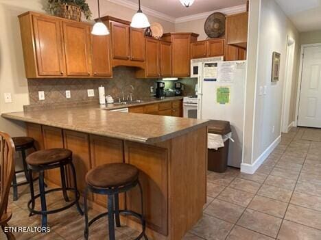 kitchen featuring white appliances, a peninsula, backsplash, and brown cabinets