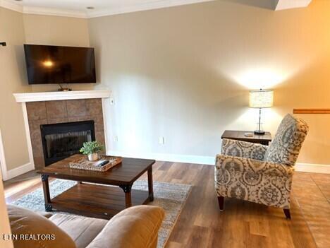 living area featuring ornamental molding, a tiled fireplace, wood finished floors, and baseboards