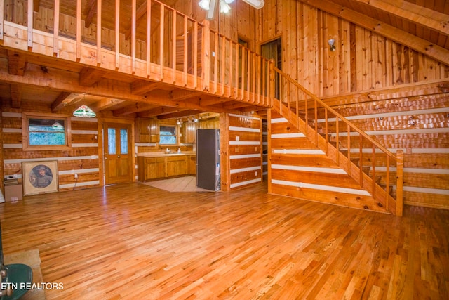 unfurnished living room with beamed ceiling, ceiling fan, high vaulted ceiling, wooden walls, and light hardwood / wood-style floors