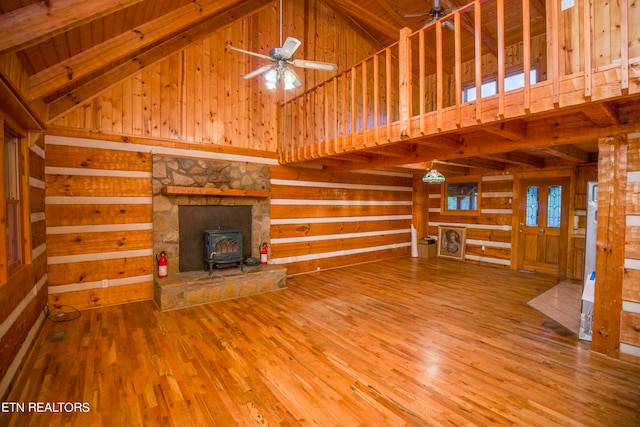 unfurnished living room featuring beamed ceiling, ceiling fan, hardwood / wood-style floors, a wood stove, and high vaulted ceiling