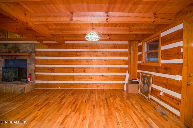 unfurnished living room with beamed ceiling, light hardwood / wood-style flooring, a wood stove, and wooden ceiling