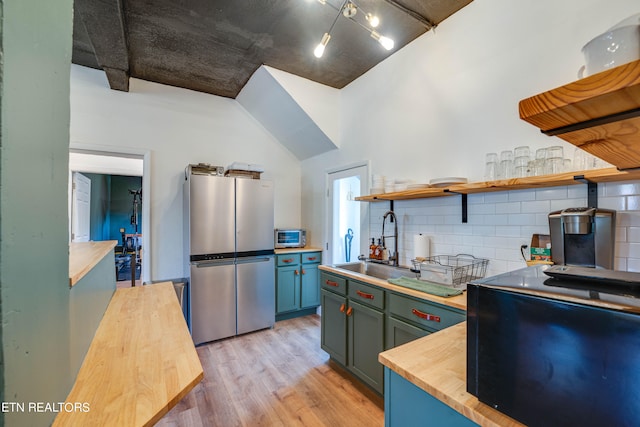 kitchen with sink, light hardwood / wood-style flooring, a high ceiling, butcher block countertops, and stainless steel fridge