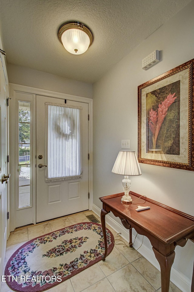 foyer entrance with a textured ceiling and light tile patterned flooring