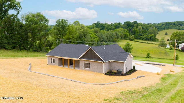 view of front of property with driveway, brick siding, a rural view, and central air condition unit