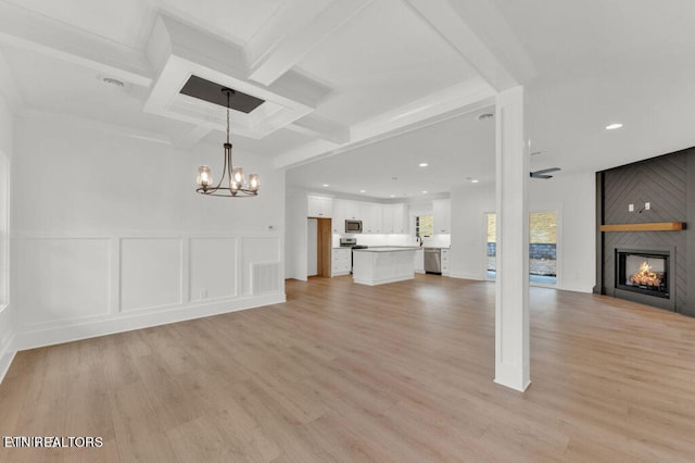 unfurnished living room featuring beam ceiling, a chandelier, light hardwood / wood-style flooring, and a large fireplace