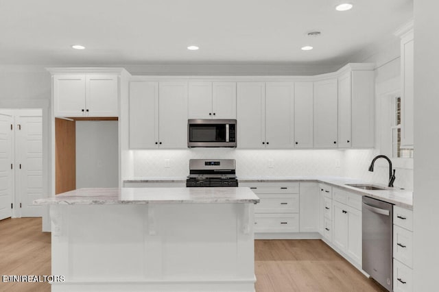 kitchen featuring appliances with stainless steel finishes, sink, light wood-type flooring, a center island, and white cabinets