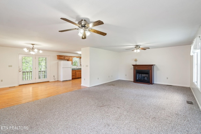 unfurnished living room featuring ceiling fan with notable chandelier and light hardwood / wood-style flooring