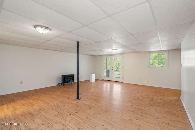 basement with french doors, a drop ceiling, light hardwood / wood-style floors, and a wood stove